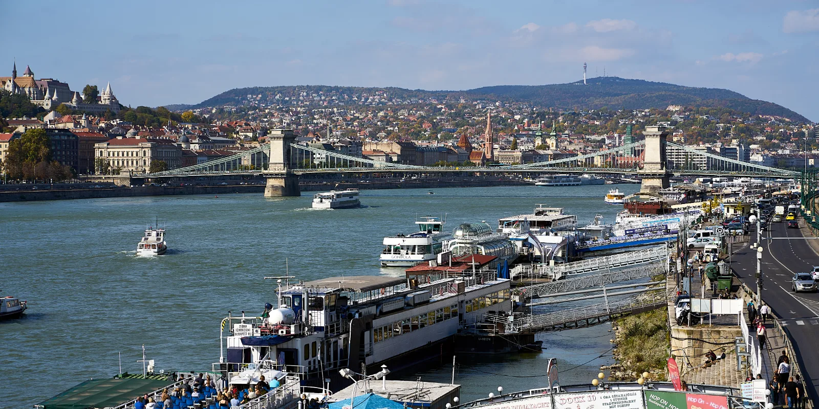 Doonau jõgi Budapestis: kaldal valged reisilaevad, taga linn, sild üle jõe ja Buda mäed