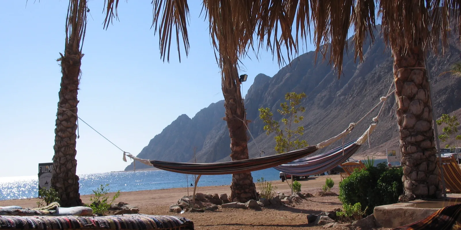 Palmid ja võrkkiik Dahabi rannal, taamal Siinai mäed ja Aqaba lahe sinine vesi