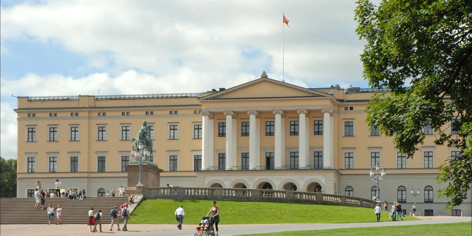 Oslo kuninglik loss kollakas päevavalguses, ees lai muruväljak ja jalutajad