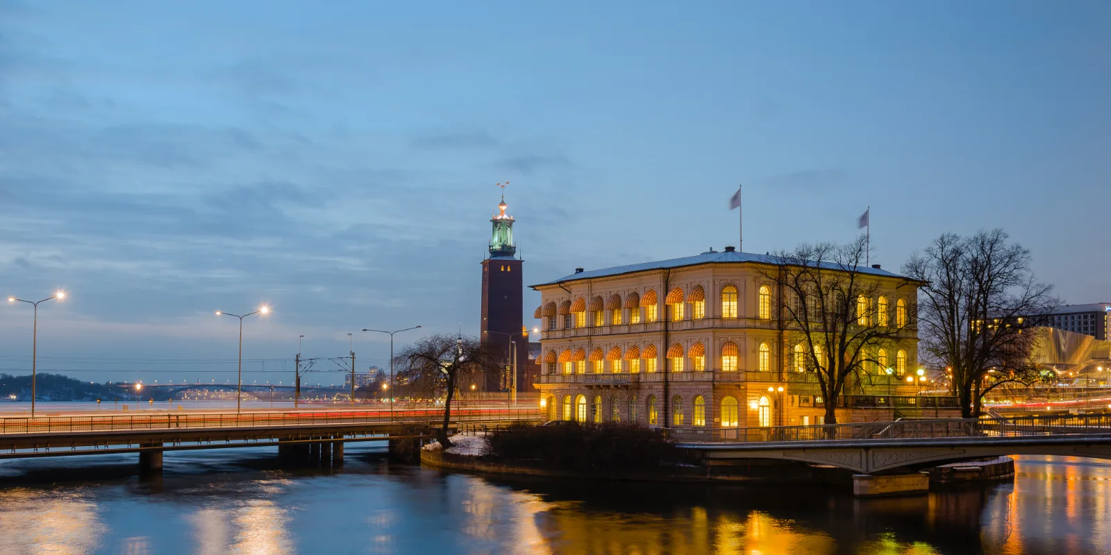 Stockholmi raekoda ja selle tornikiiver sinisel õhtutunnil, soojalt valgustatud aknad peegelduvad vees.